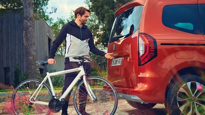 Човек крева велосипед пред задниот дел на Kangoo Passenger.