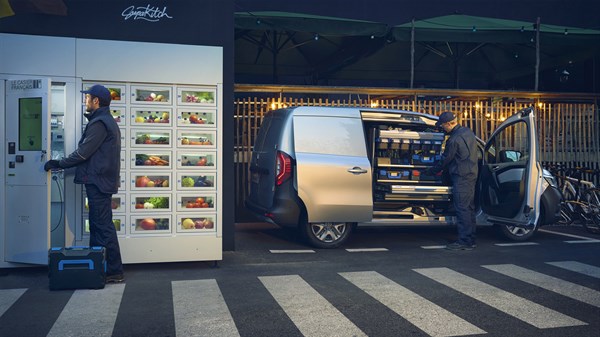 Kangoo Van паркирано пред ладилник-витрина, двајца работници земаат или товарат стока од возилото.